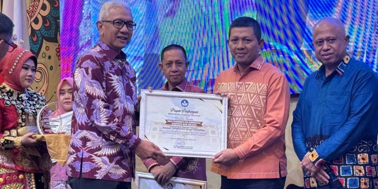 Penjabat Gubernur Gorontalo, Rudy Salahuddin saat menyerahkan Piagam Penghargaan kebijakan Merdeka Belajar kepada Kepala Dinas Pendidikan dan Kebudayaan Kabupaten Bone Bolango, Adrien Andjar di Hotel Aston Kota Gorontalo, Minggu (20/10/2024). (Foto Dok Dinas Pendidikan dan Kebudayaan)