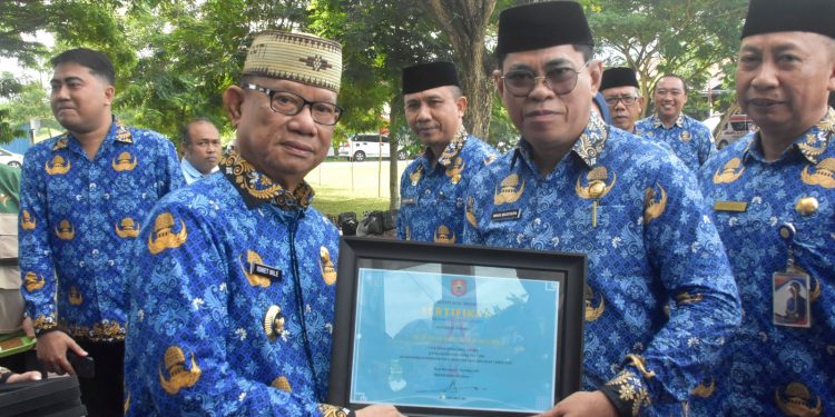 Bupati Bone Bolango, Ismet Mile, saat menyerahkan Penghargaan TOP IPASN Excellence Award 2025 kepada Sekda Iwan Mustapa di sela Upacara HUT Korpri ke-54, HUT PGRI, dan Hari Guru ke-80 di Lapangan Alun-Alun Bone Bolango, Senin (1/12/2025). (F.Indra/Diskominfo)