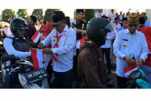 Bupati Ismet Mile dan Wabup Risman Tolingguhu saat membagikan bendera merah putih kepada masyarakat, Senin (3/8/2026). (F.Indra/Diskominfo)
